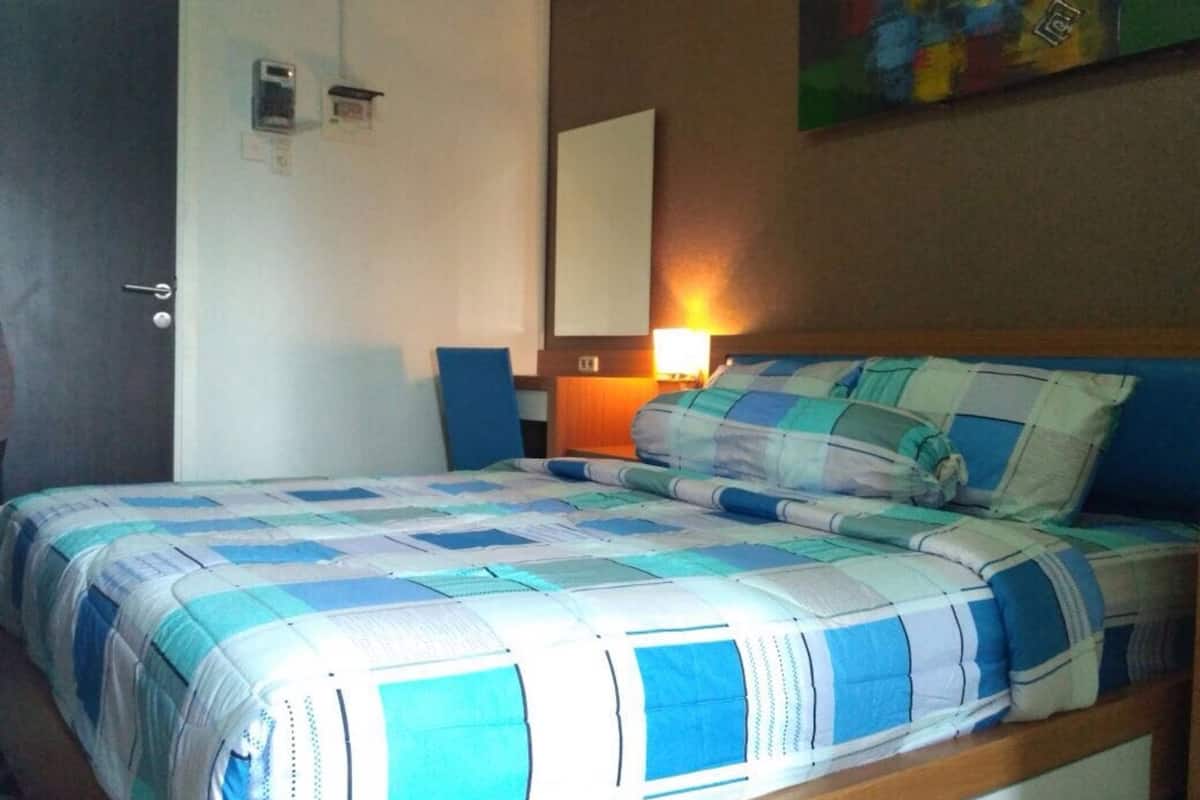 A bedroom with a bed, a chair, a bedside table, a lamp, and a painting on the wall.