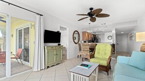 A spacious living room with a television, a ceiling fan, and a dining area with wicker furniture. - Gulfside Comfort – Beach Castle #4 by RVA (Longboat Key)