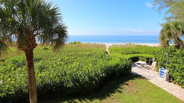 A pathway leading to a beach with a palm tree and green bushes. - Gulfside Comfort – Beach Castle #4 by RVA (Longboat Key)