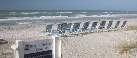 A beach resort sign with a row of beach chairs and the ocean in the background.