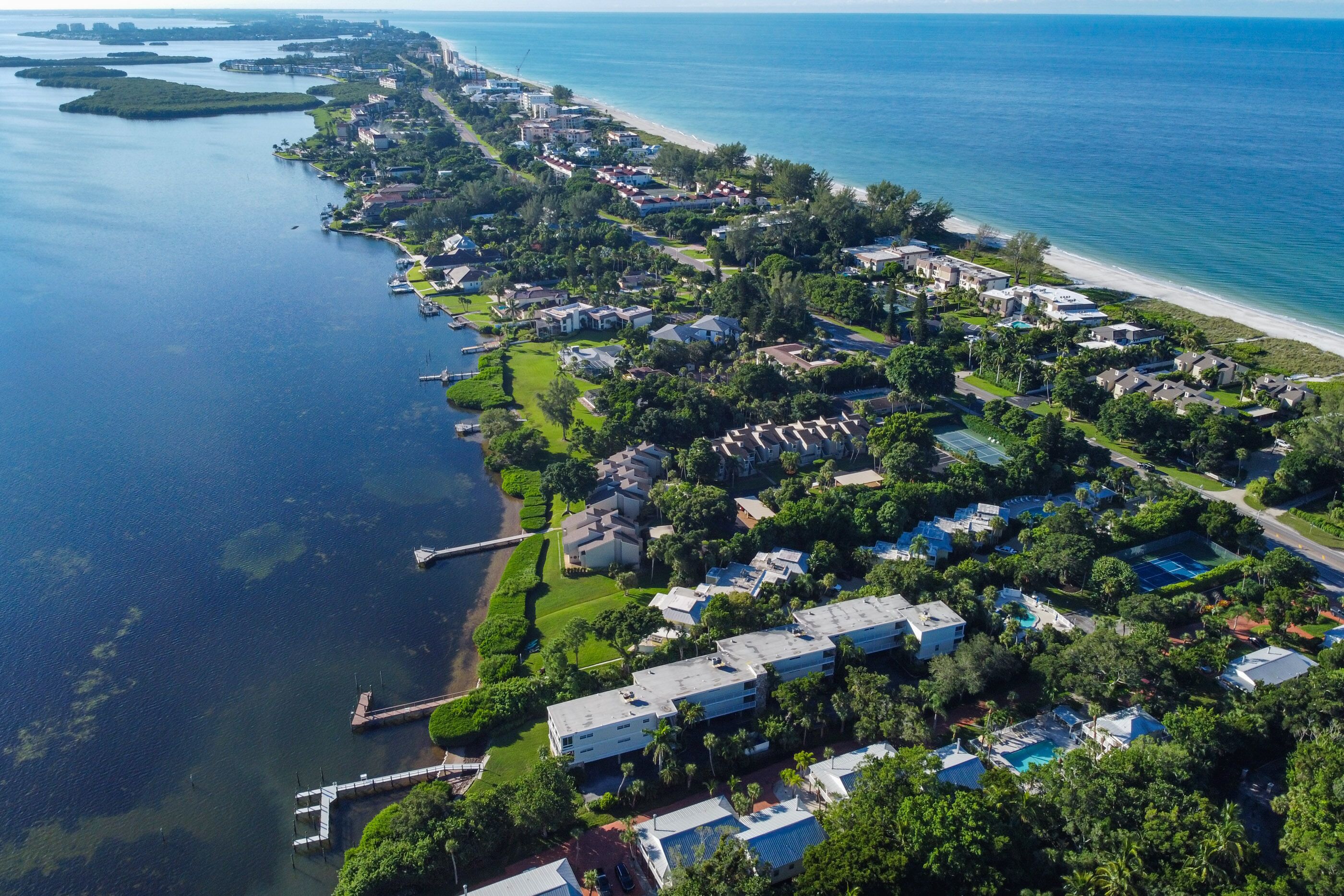 An aerial view of a coastal residential area with houses, a marina, and a beach.