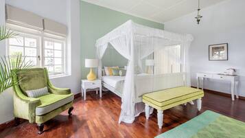 A room with a four-poster bed, a green armchair, a bedside table with a lamp, and a small bench.