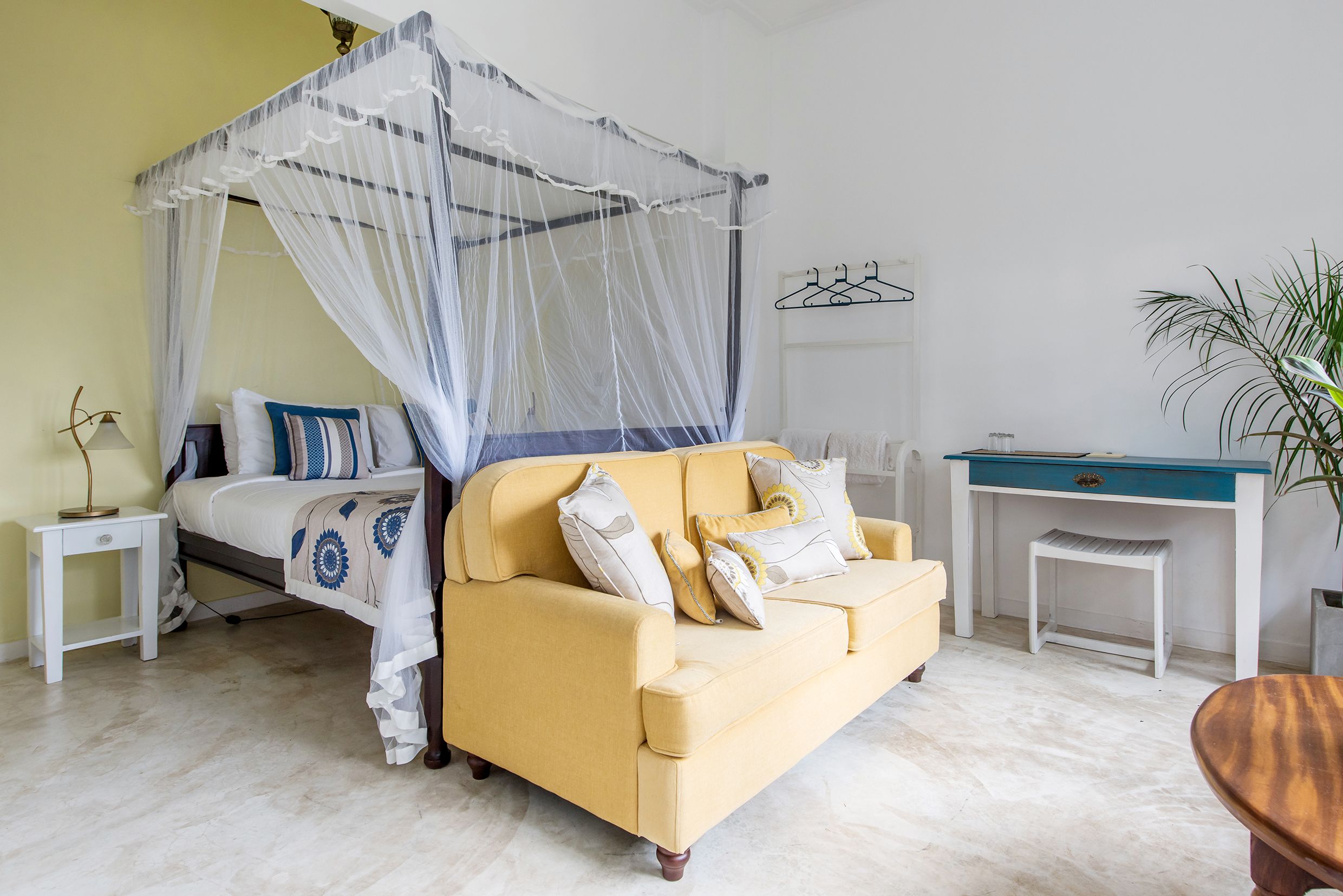 A bedroom with a bed, a yellow sofa, a desk, and a plant.
