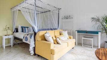 A bedroom with a bed, a yellow sofa, a desk, and a plant.