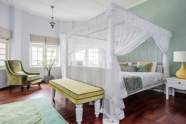 A bedroom with a canopy bed, a green armchair, a bench, and a bedside table with a lamp. - Ashburnham Estate (Rattota)