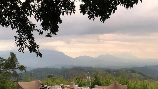 An outdoor dining setup with a table set for six, surrounded by chairs, overlooking a mountainous landscape. - Ashburnham Estate (Rattota)