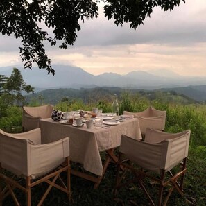 An outdoor dining setup with a table set for six, surrounded by chairs, overlooking a mountainous landscape. - Ashburnham Estate (Rattota)