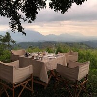 Un montaje para comidas al aire libre con una mesa dispuesta para seis personas, rodeada de sillas, con vistas a un paisaje montañoso.