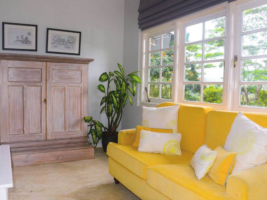 Een kamer met een gele bank, een houten kast en een raam met uitzicht op groen.
