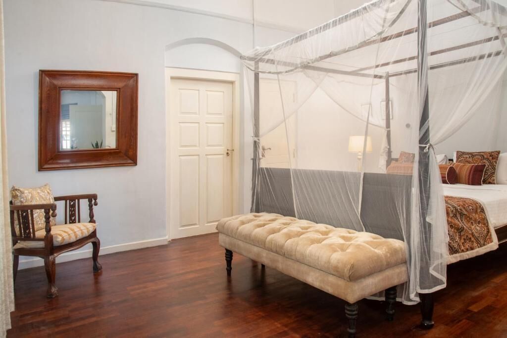 A bedroom with a four-poster canopy bed, a wooden bench, a chair, and a mirror on the wall.