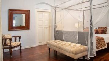 A bedroom with a four-poster canopy bed, a wooden bench, a chair, and a mirror on the wall.