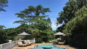 A swimming pool with lounge chairs and umbrellas, surrounded by trees and a white fence. - Ashburnham Estate (Rattota)
