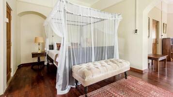 A bedroom with a canopy bed, a bench, a nightstand, and a lamp.