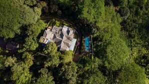 An aerial view of a property surrounded by dense forest, featuring a large house with multiple roofs, a swimming pool, and a well-maintained garden. - Ashburnham Estate (Rattota)