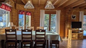 A wooden cabin with a dining area featuring a table, chairs, and a television.