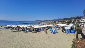A beach with numerous umbrellas and sun loungers, a playground, and a view of the sea and distant hills. - "A TASTE OF PROVENCE" Among Olive Trees and the Sea (Terzorio)