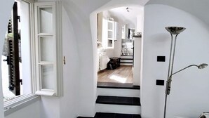 A staircase leading to a kitchen area with white walls, a black and white tiled floor, and a modern light fixture. - "A TASTE OF PROVENCE" Among Olive Trees and the Sea (Terzorio)