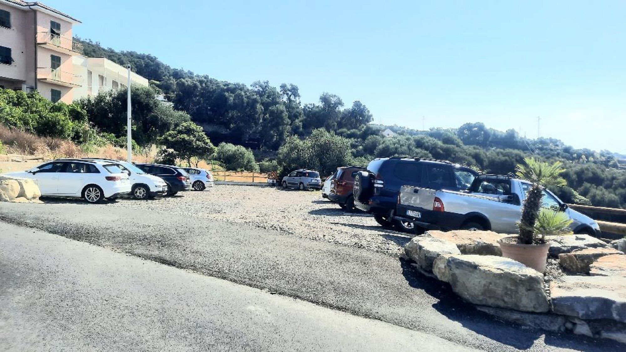 Uma área de estacionamento com vários carros, um edifício com varandas e montanhas ao fundo.