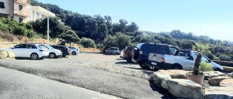 Uma área de estacionamento com vários carros, um edifício com varandas e montanhas ao fundo.