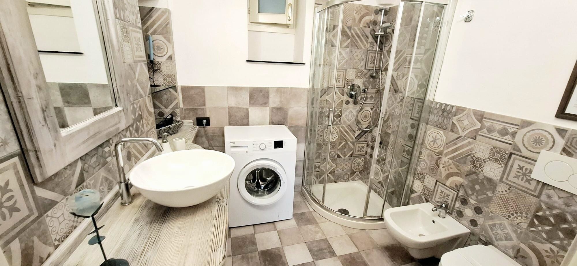 Een badkamer met een wastafel, wasmachine, bidet en douche.