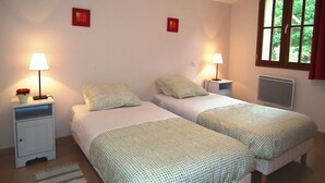 Une chambre avec deux lits, chacun étant équipé d  ’un oreiller et d’une table de chevet avec une lampe. Une fenêtre offre une vue sur la verdure environnante.