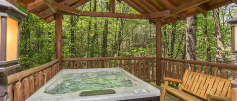 A hot tub on a wooden deck with a wooden railing, surrounded by a forest.
