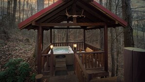 En træhytte med jacuzzi og en stol udenfor, omgivet af træer.