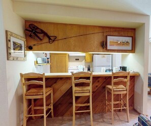 A kitchen with wooden bar stools, a microwave, and a refrigerator.