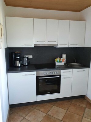 A compact kitchen with white cabinets, a black countertop, a coffee maker, a kettle, and a sink.
