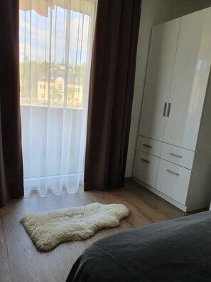 Une chambre dotée d’une grande armoire, d’un tapis moelleux et offrant une vue sur les bâtiments environnants.