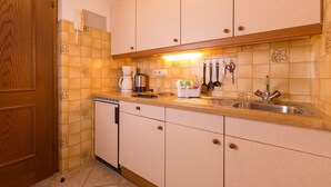 A compact kitchen with wooden cabinets, a built-in dishwasher, and a countertop with a coffee maker, kettle, and utensils. - Apartment garden view - Apartment house Roland (Strobl)