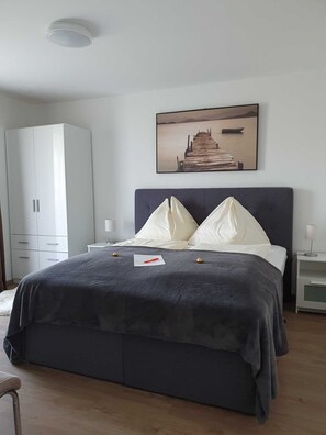Une chambre à coucher avec un lit, une table de chevet, une armoire blanche et un tableau représentant une jetée.