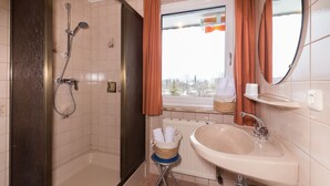 A bathroom with a shower, a sink, a window with curtains, and a mirror. - Apartment garden view - Apartment house Roland (Strobl)