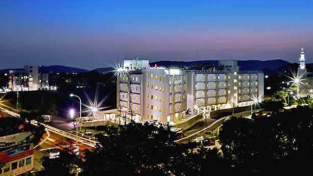 Un hotel de varios pisos con una torre destacada, rodeado de árboles e iluminado por farolas.