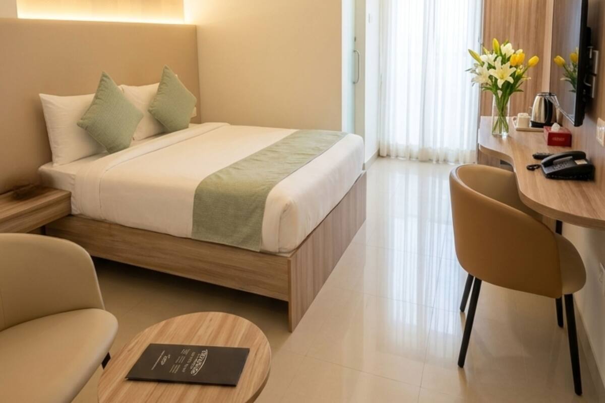 Ein Hotelzimmer mit Bett, Nachttisch, Sessel, Schreibtisch und einem Flachbildfernseher.