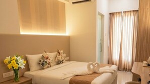 Una habitación de hotel con una cama, una mesita de noche, un jarrón de flores, un letrero, un baño con lavamanos y una ventana con cortinas.