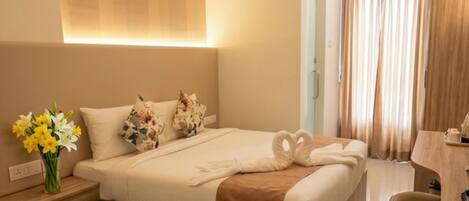 Una habitación de hotel con una cama, una mesita de noche, un jarrón de flores, un letrero, un baño con lavamanos y una ventana con cortinas.