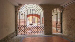 Un portail en arc surmonté d’une grille métallique, qui donne sur un couloir au sol carrelé et aux murs en briques.