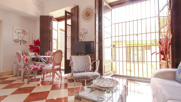 Un salon avec un sol à carreaux, un coin repas avec une table et des chaises, un fauteuil à motifs, un téléviseur et une grande fen être donnant sur un beau paysage.