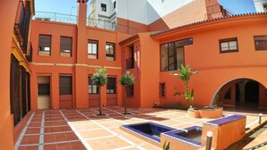 Une cour extérieure aux murs orange, au sol carrelé et agrémentée de plantes en pot.