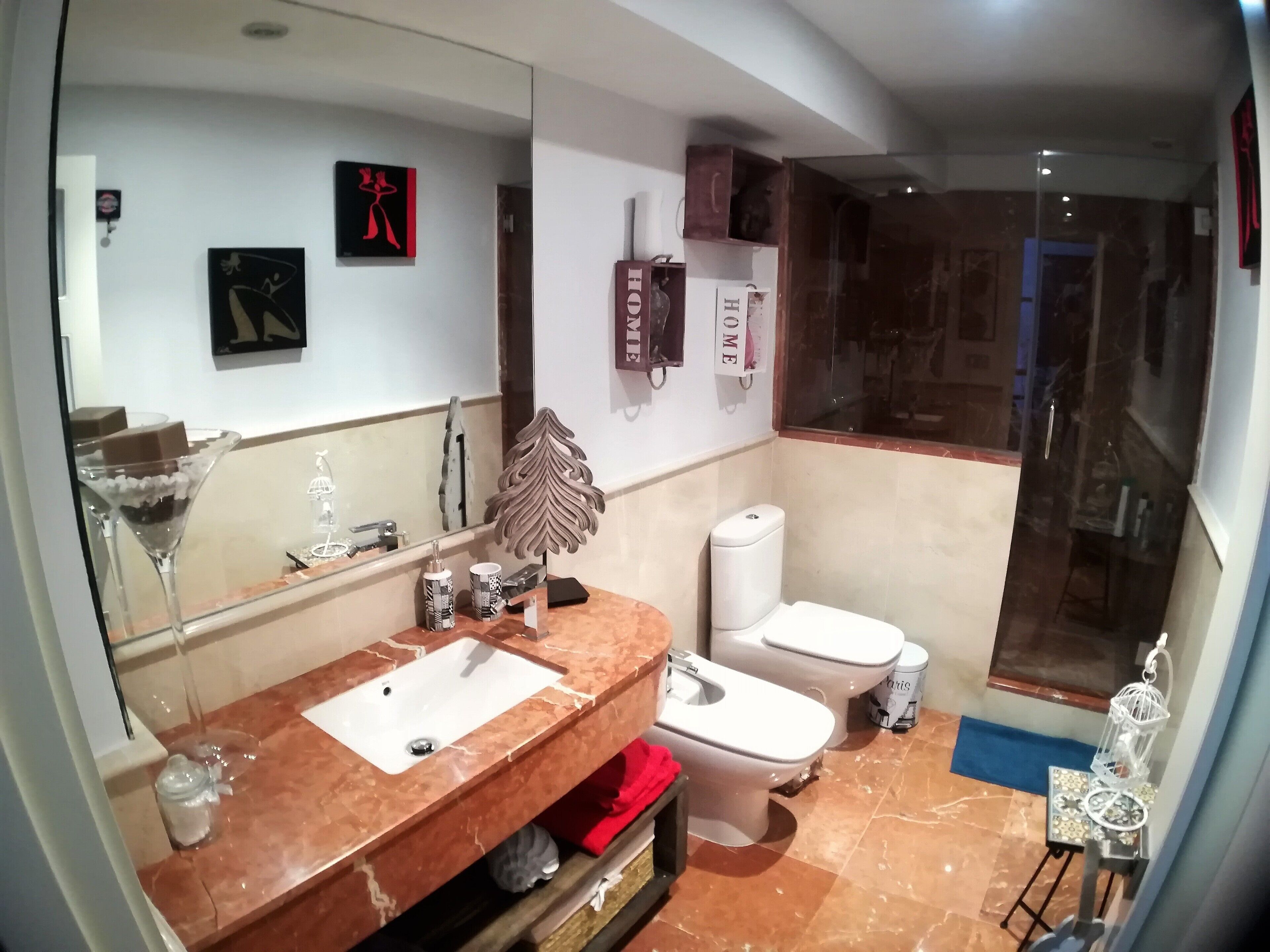 Une salle de bain moderne avec un lavabo en marbre, deux toilettes, un grand miroir et un espace douche.