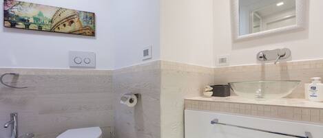 A bathroom with a toilet, bidet, and sink. There is a painting on the wall and a mirror above the sink.