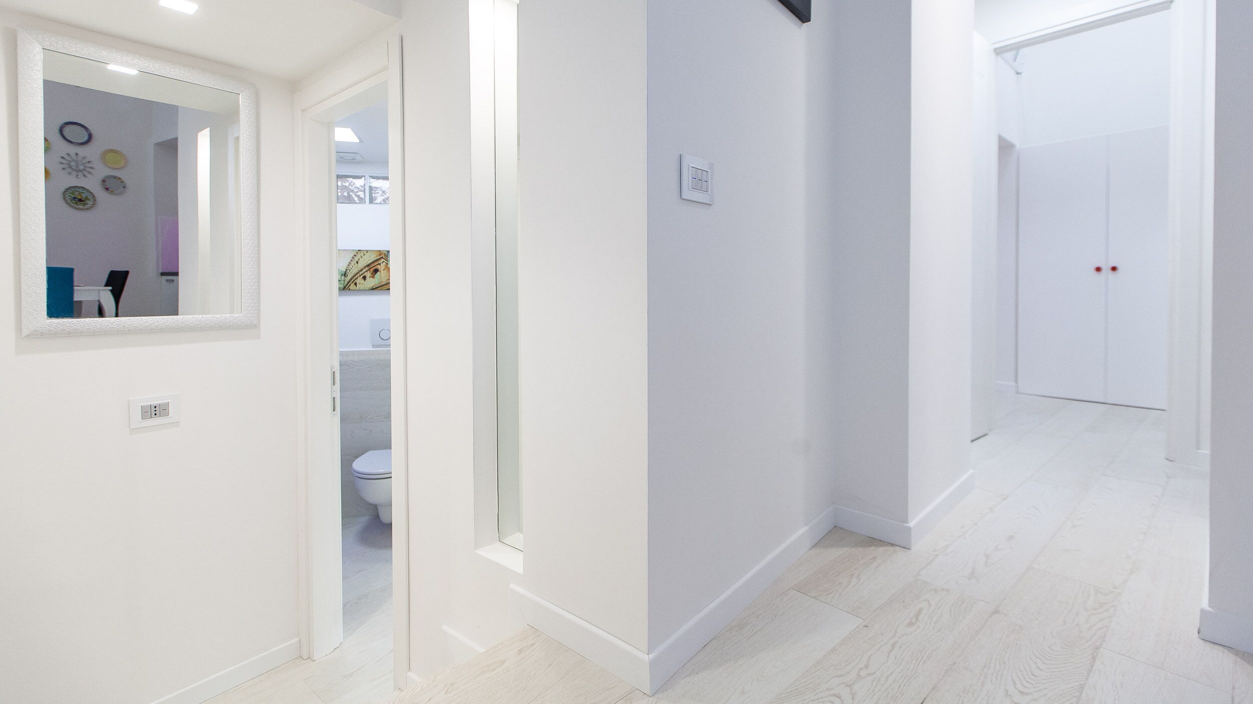 A hallway with white walls, a mirror, and a door leading to a bathroom.