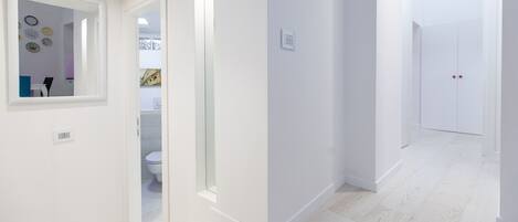 A hallway with white walls, a mirror, and a door leading to a bathroom.
