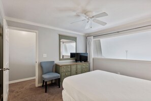 Een slaapkamer met een bed, een stoel, een dressoir, een televisie en een plafondventilator.