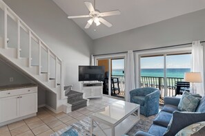 A living room with a TV, sofa, and a balcony with a view of the ocean.
