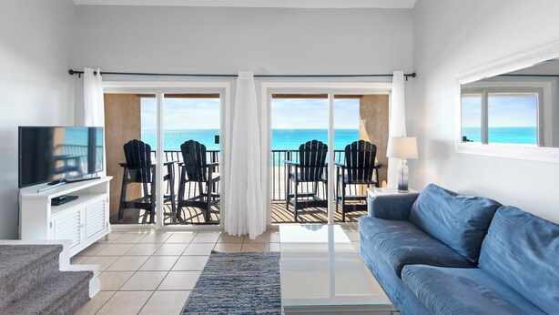 Ein modernes Wohnzimmer mit großem Fernseher, einer Couch und einem Balkon mit Sitzgelegenheiten und Meerblick.