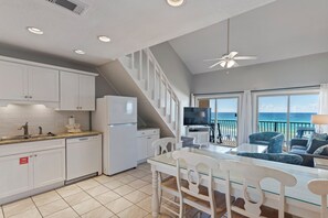A modern kitchen with white cabinets, a dining area with a glass table, and a balcony with a view of the ocean.