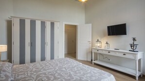 A bedroom with a bed, wardrobe, bedside table, lamp, TV, and a door leading to another room.