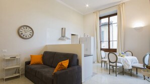 A modern living room with a sofa, a dining table with chairs, a clock, and a window with curtains.